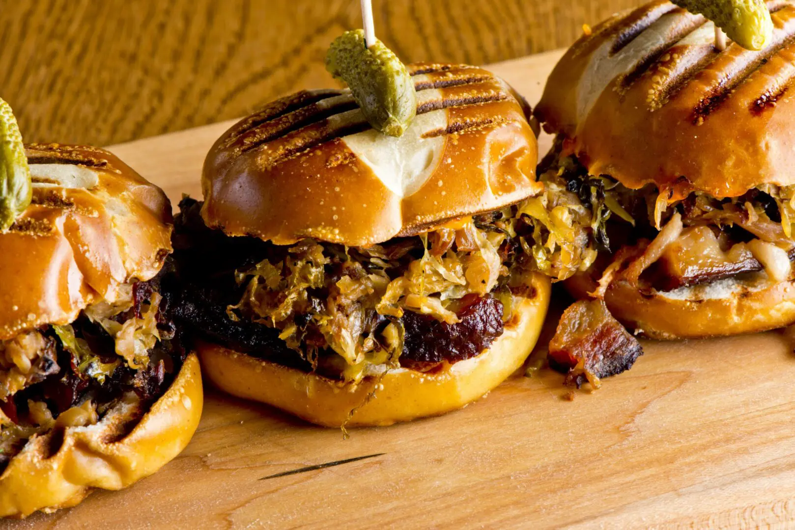Three grilled BBQ sliders with pickles and onions
